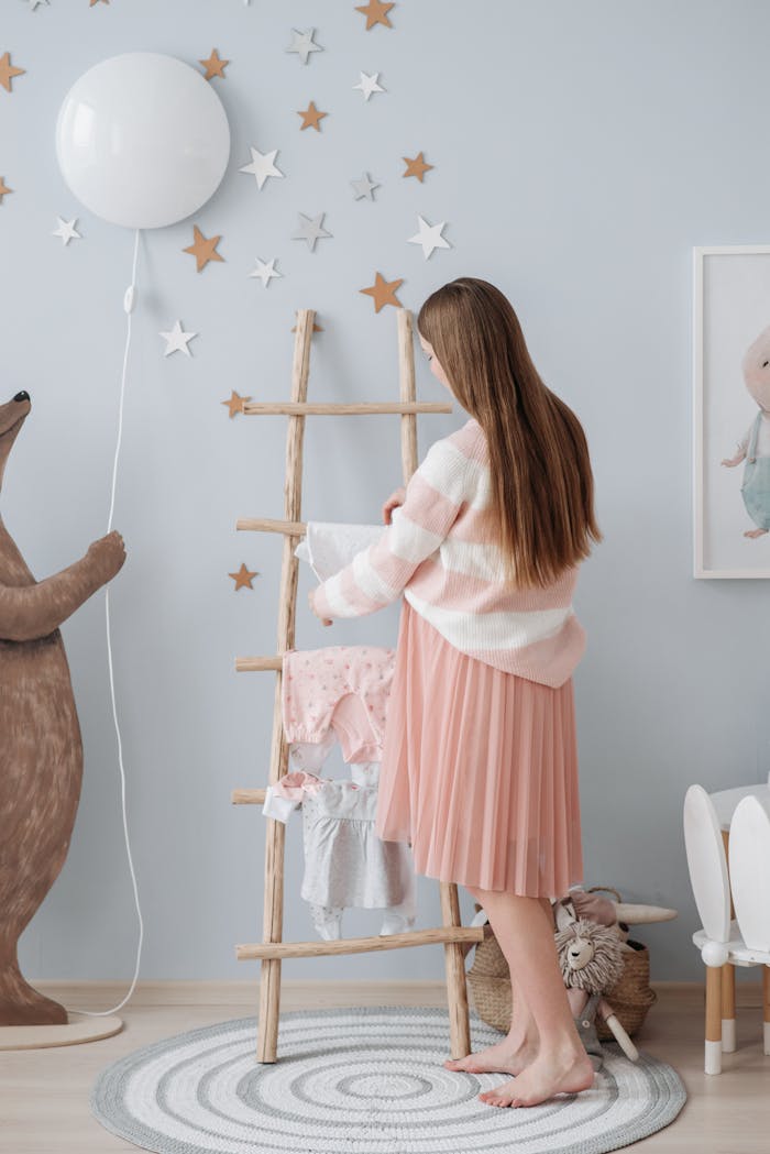 Home Pregnant woman arranging baby clothes in a softly decorated nursery room with pastel colors.